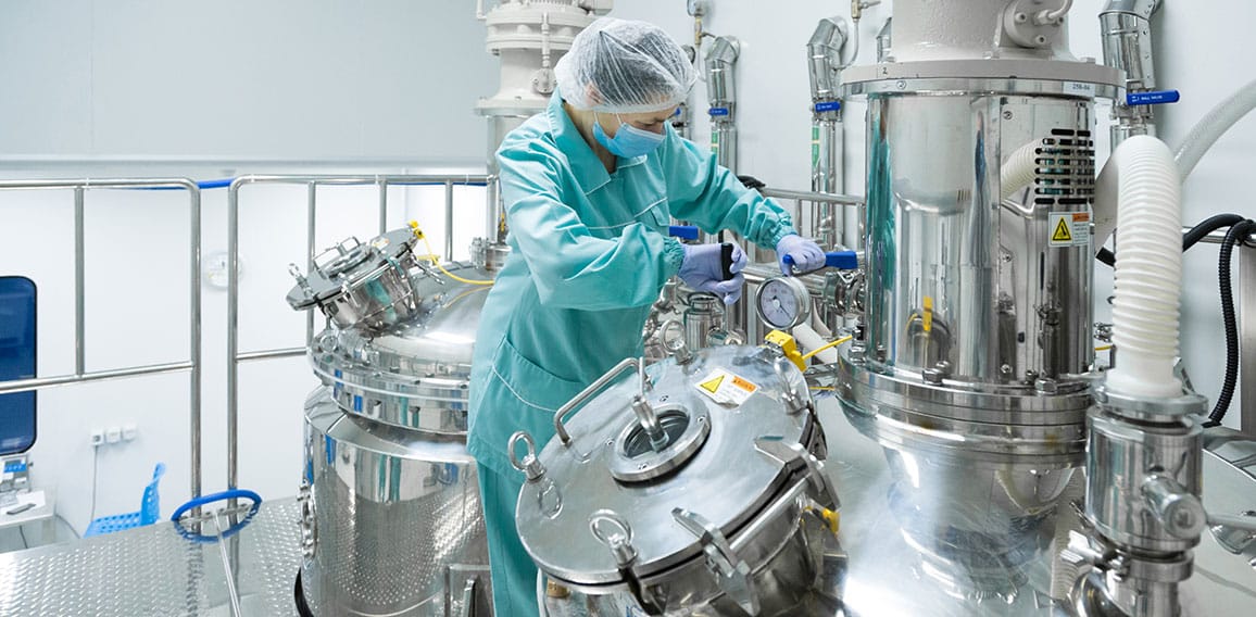 Pharmaceutical factory woman worker in protective clothing operating production line in sterile environment