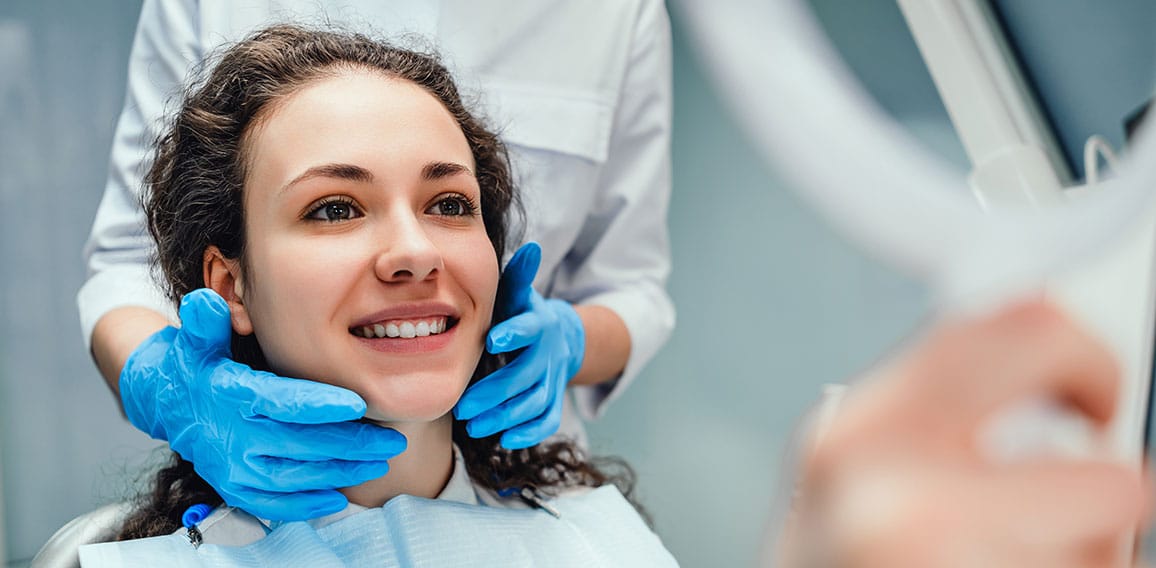 A woman is sitting at a dentist's reception. She looks in the mi