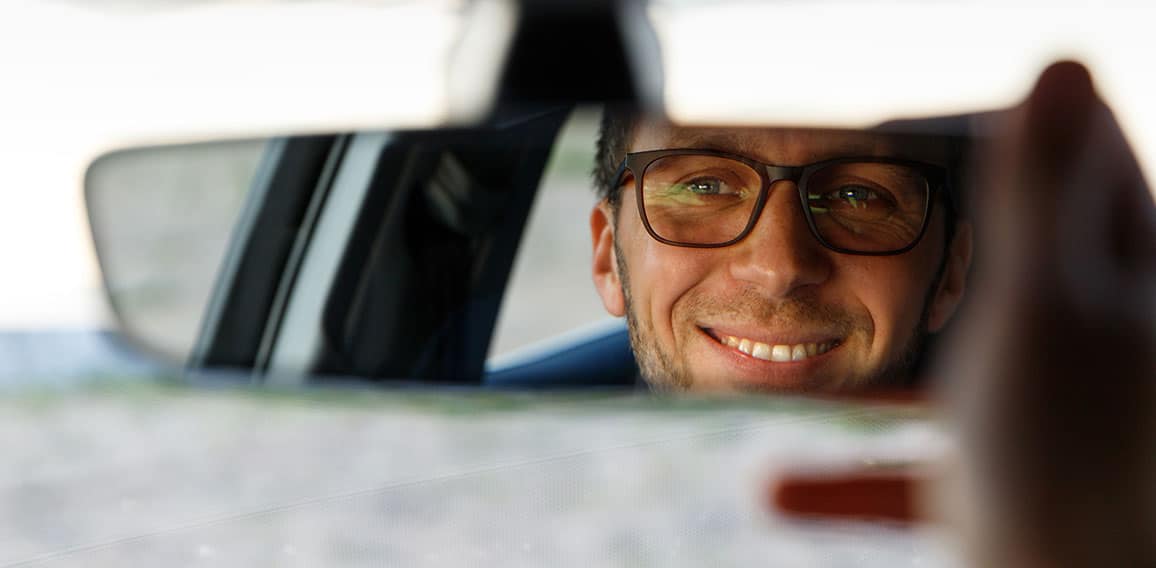 Cheerful man adjusting mirror while sitting in his car, looking