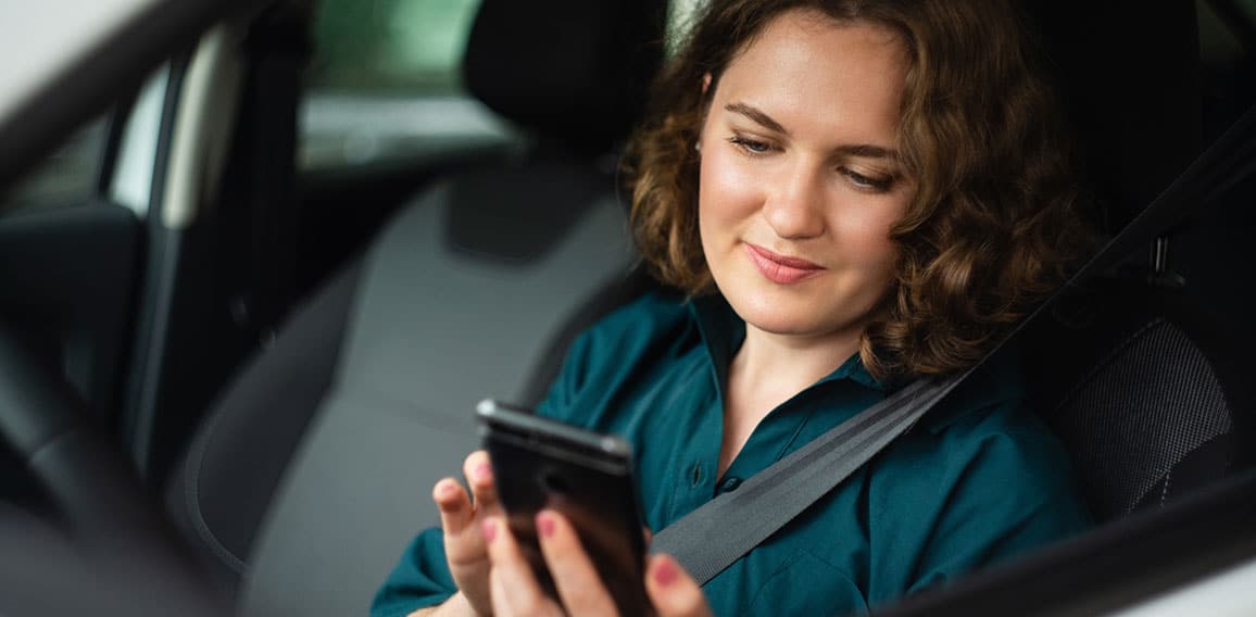 Woman driver sitting in car and looking at smartphone screen