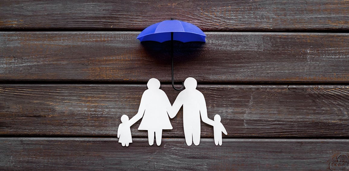 Health insurance concept. Family cutout under umbrella on dark wooden background top-down copy space