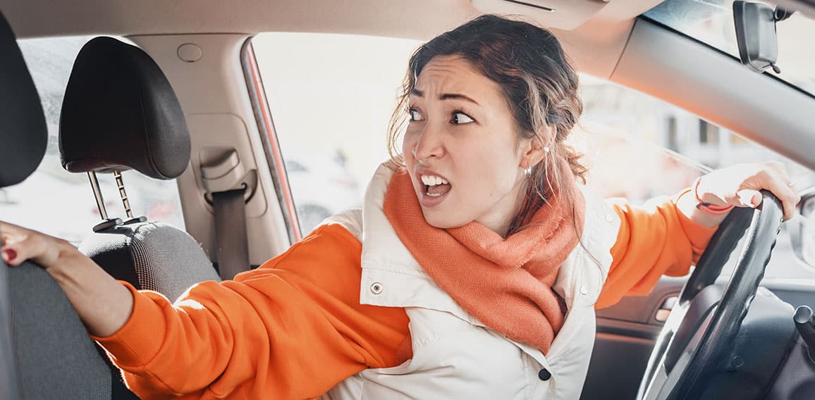 The annoyed female driver was backing up and accidentally hit a parked car. Accident and insurance