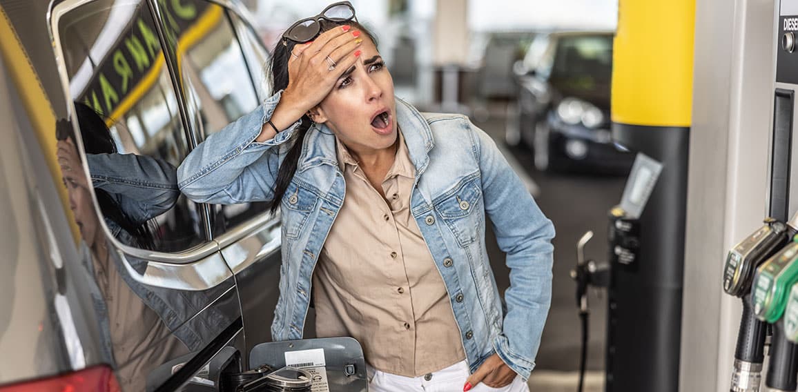 Woman refuelling the tank of her car with diesel looks shocked with mouth open seeing the high price of fuel.