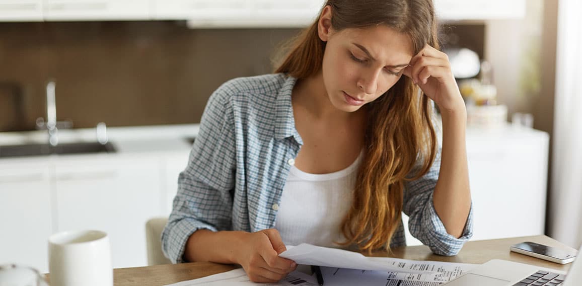 Indoor shot of casually dressed young woman holding papers in her hands, calculating family budget, trying to save some money to buy new bicycle to her son, having stressed and concentrated look