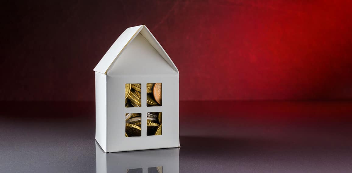 House model with Euro coins over red background with copy space