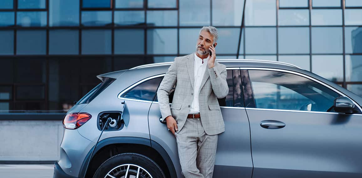 Businessman holding smartphone while charging car at electric vehicle charging station, closeup.