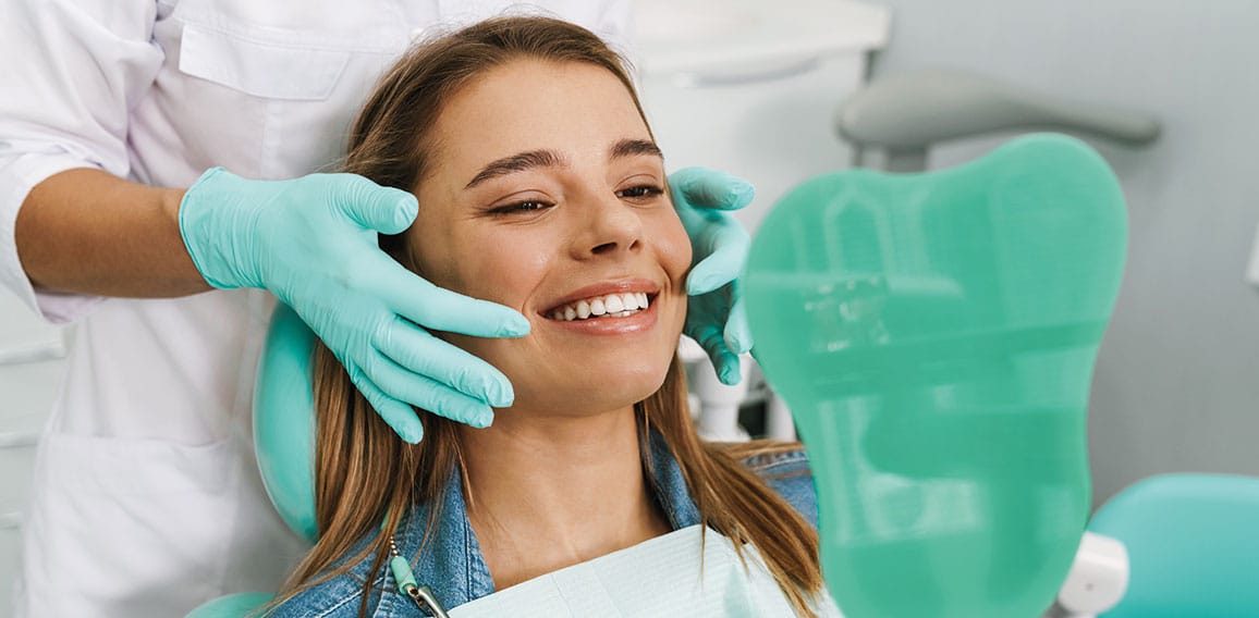 European young woman smiling while looking at mirror in dental c