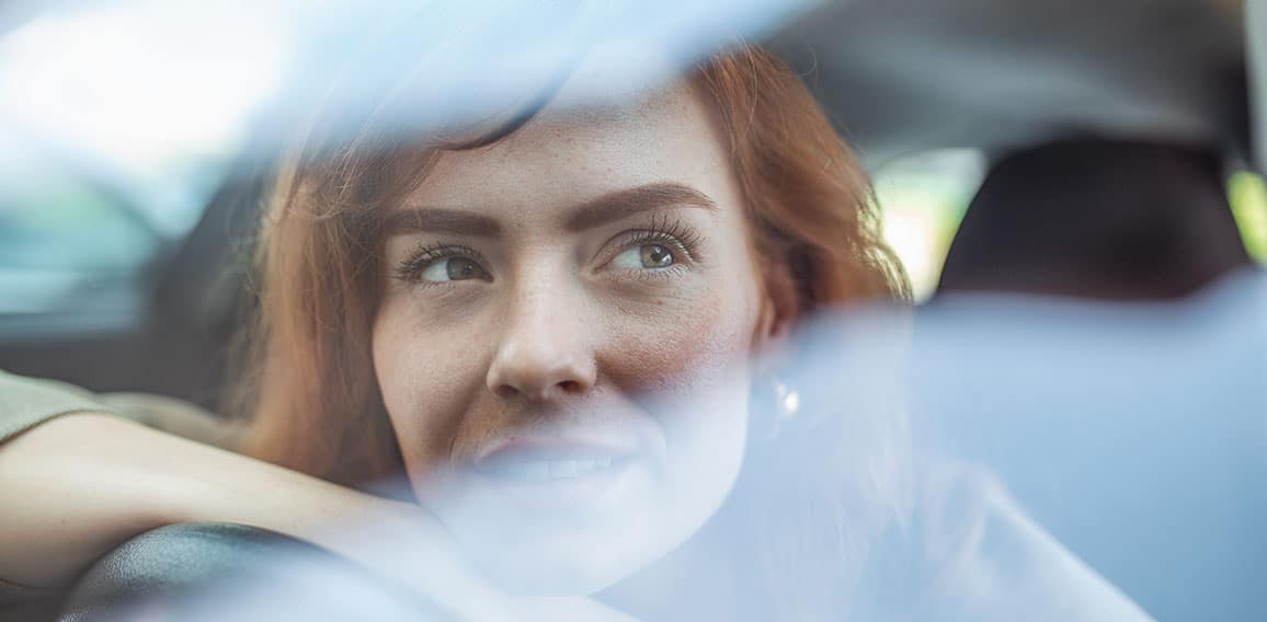 Young Woman Embracing Her New Car. Excited young woman and her new car indoors. Young and cheerful woman enjoying new car hugging steering wheel sitting inside