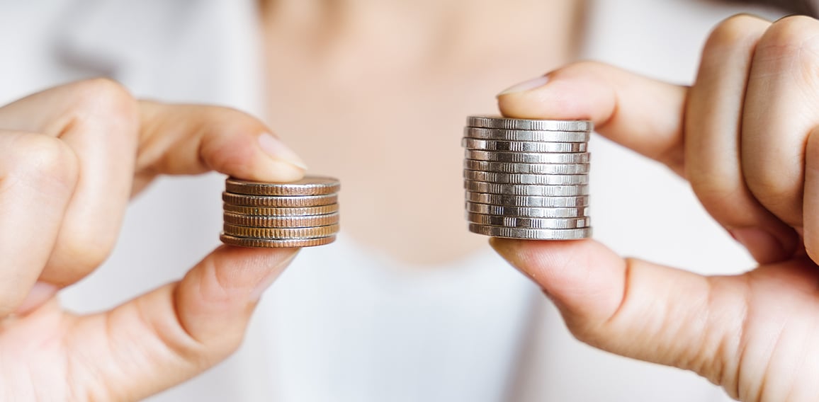 Hands compare two piles of coins of different sizes.