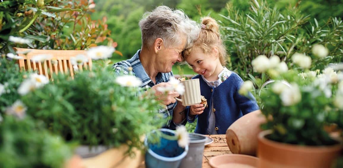 Senior grandmother with small granddaughter gardening on balcony in summer, resting.