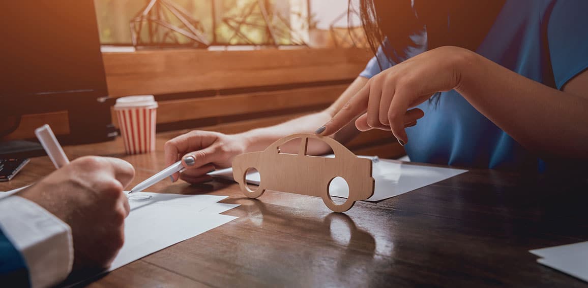 Man signing a car insurance policy, the agent is holding the wooden car model.