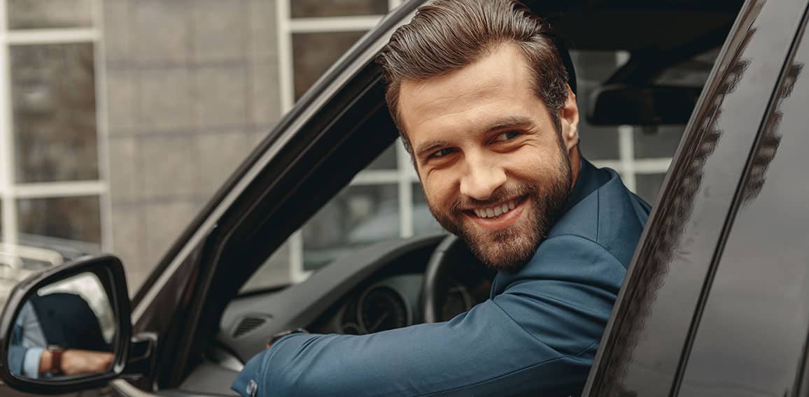 Laughing Caucasian business man in suit looking away in salon of automobile