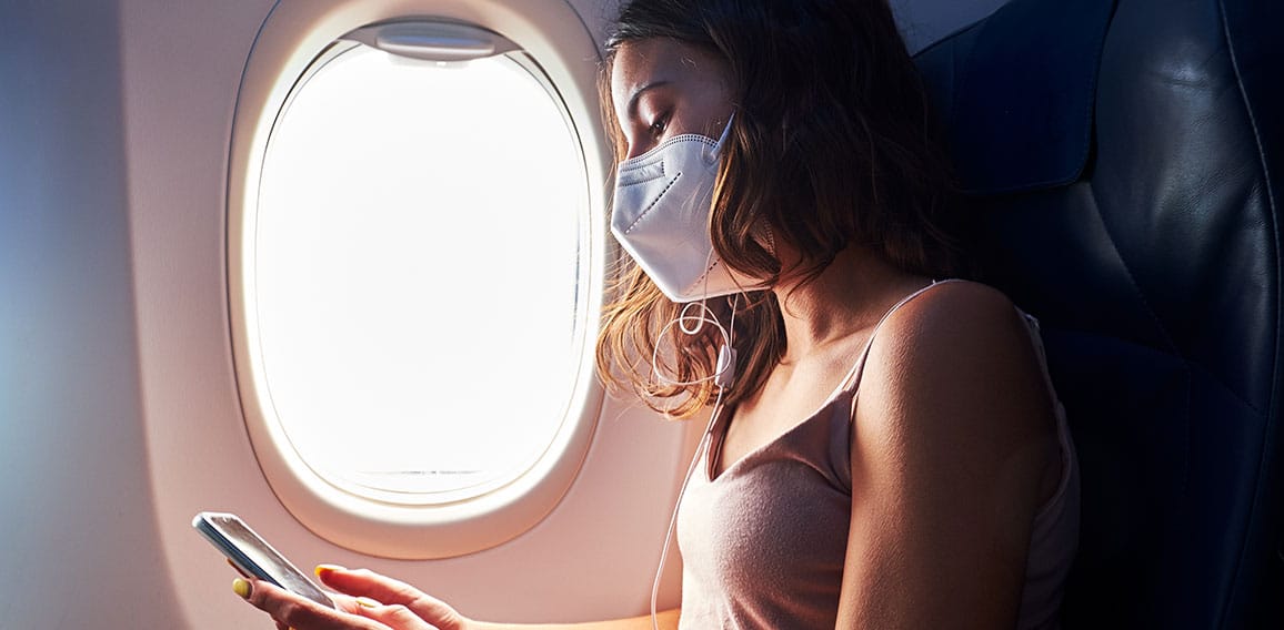 young girl wearing face mask using smartphone while traveling on