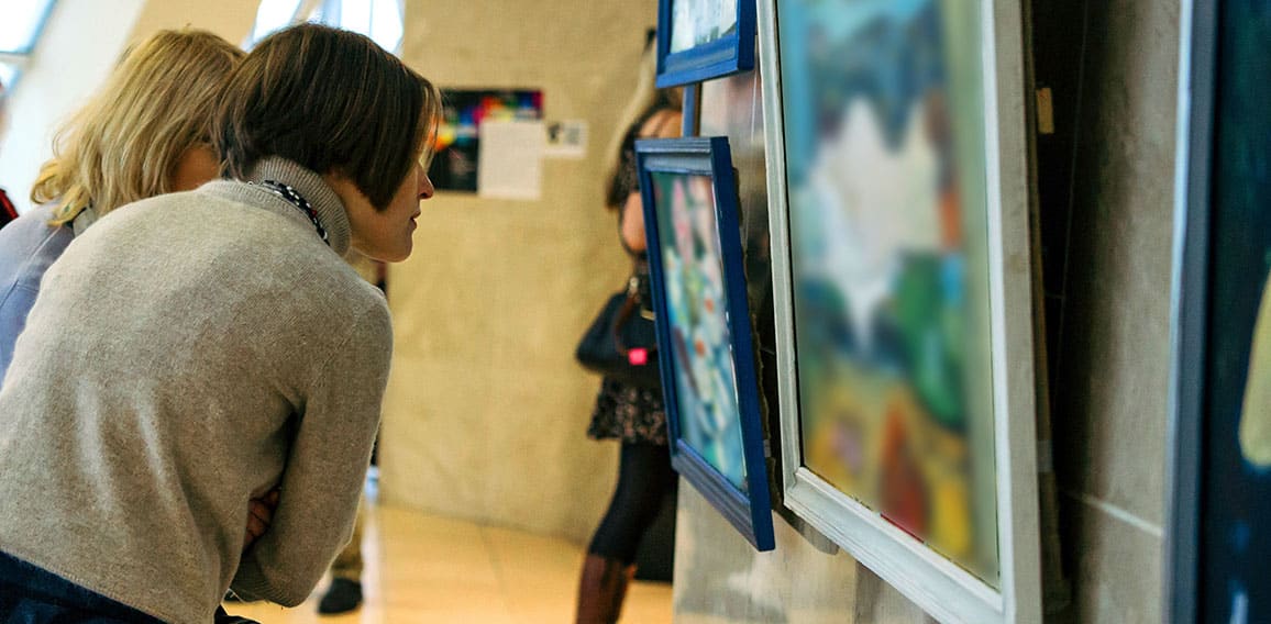 rear view of younga caucasian woman stading in an art gallery in front of two large colorful paintings