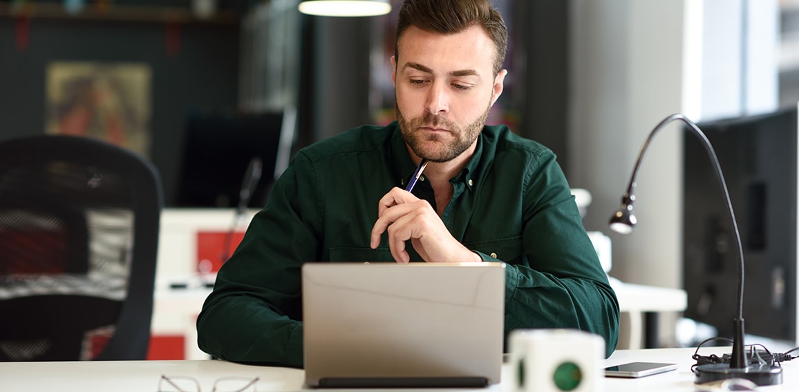 Young man studying with laptop computer on white desk.