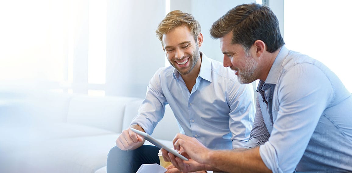 Young and mature businessmen smiling while using a digital table