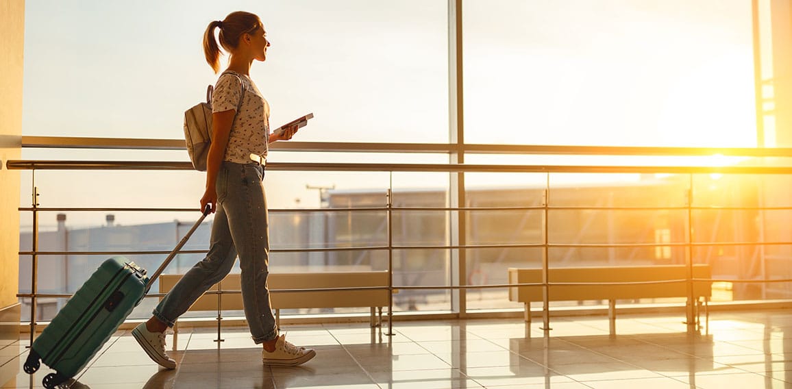 young woman goes  at airport at window with suitcase waiting for plane