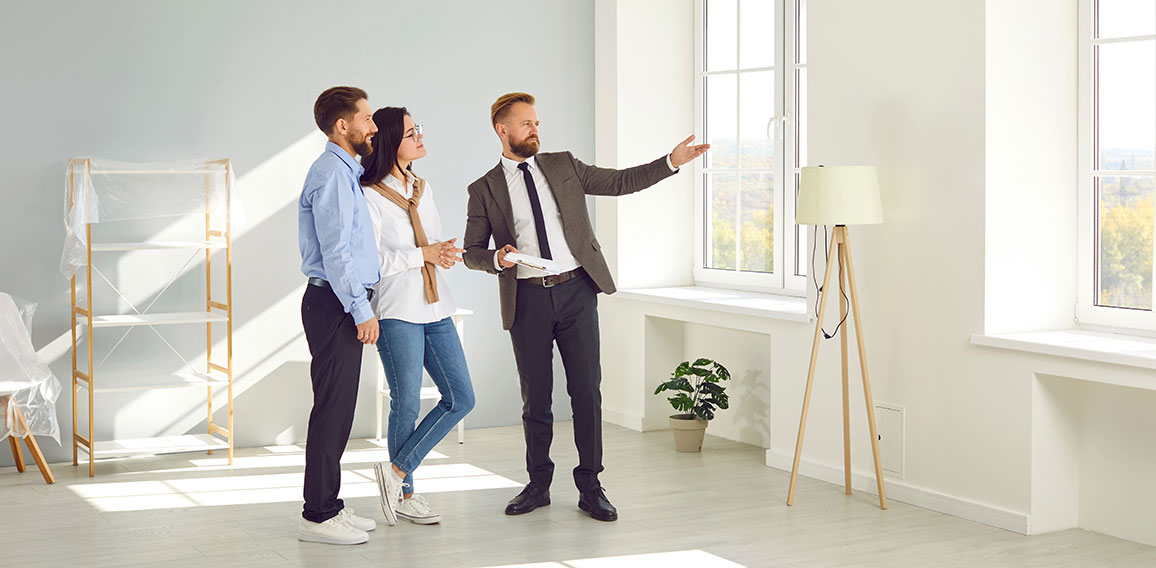 Real estate agent young man showing new big modern flat to couple of buyers or tenants.