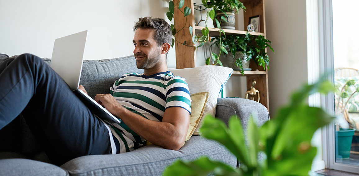 Smiling young man using a laptop on his sofa