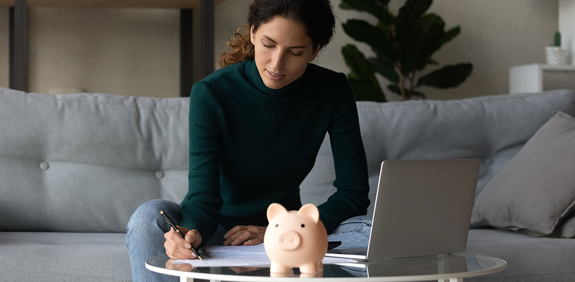 Satisfied woman checking finances, sitting at table with piggy bank