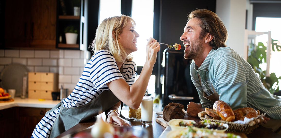 Beautiful young couple is smiling while cooking together in kitchen at home