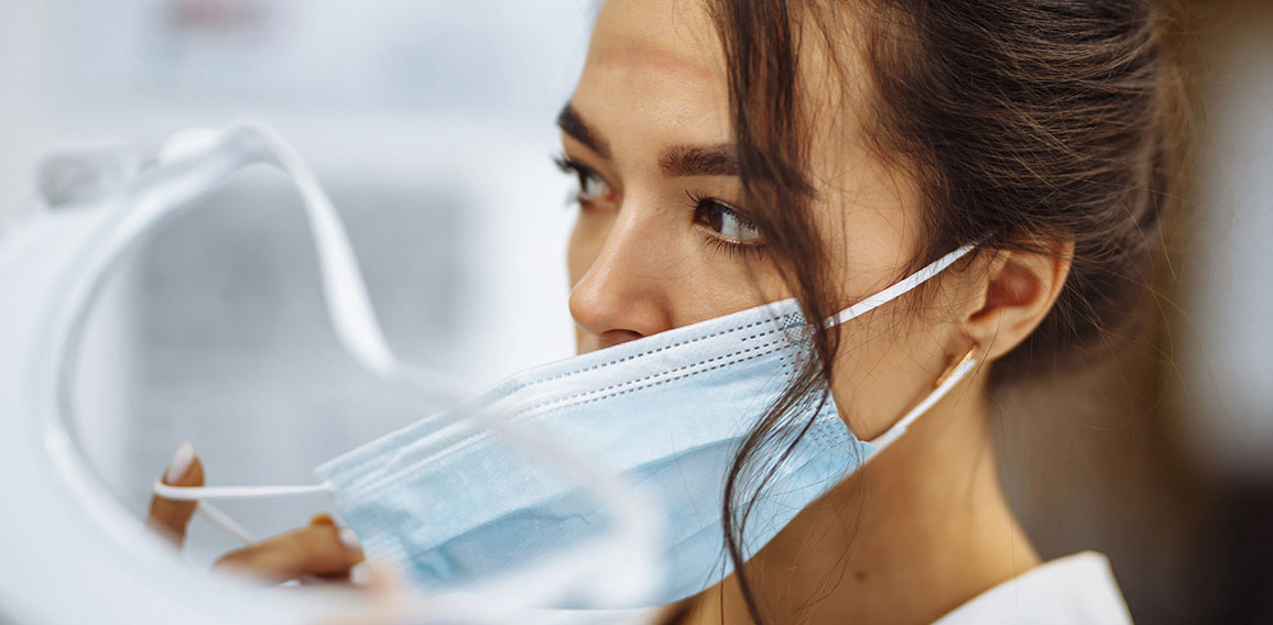 Tired nurse takes off a protective face shield and medical mask after a tough working shift at the hospital. Female doctor fights the coronavirus pandemic working hard overtime and being exhausted.