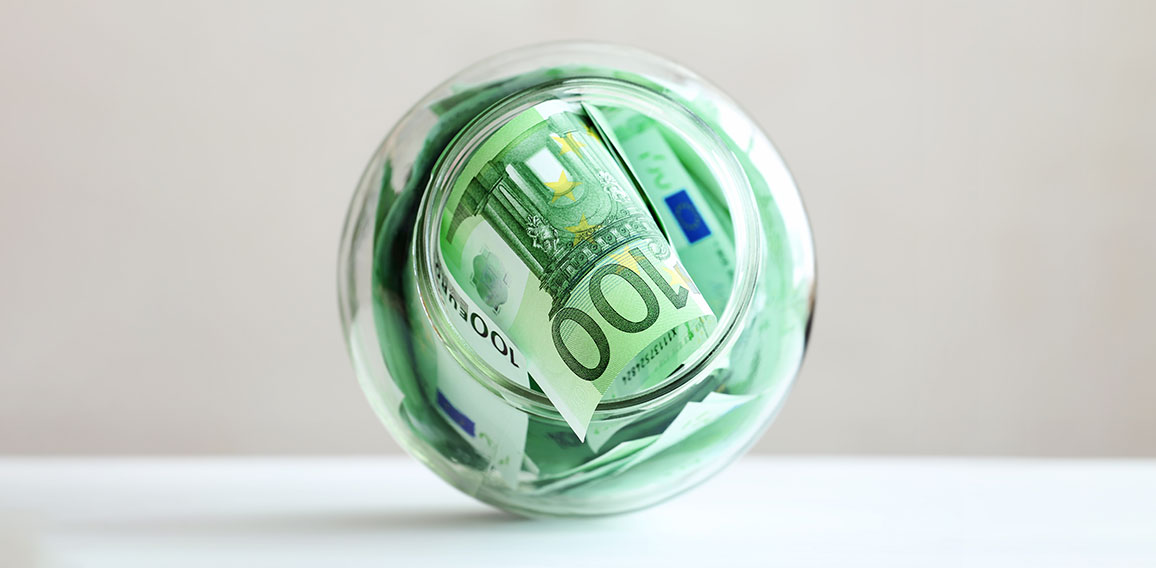 Euro banknotes in a glass jar on a grey background