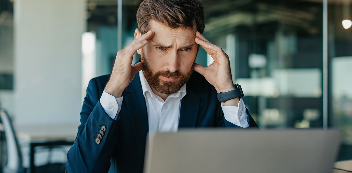 Depressed middle aged businessman looking at laptop and touching head, suffering from headache or having problems