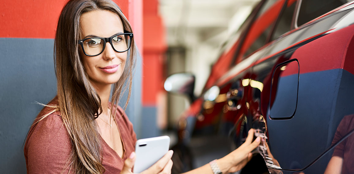 Portrait of young woman with scratched car at underground parking lot