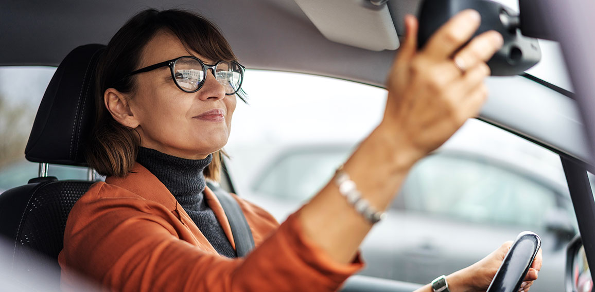 Adult caucasian businesswoman in glasses adjusting the rearview mirror while sitting at the wheel of a car