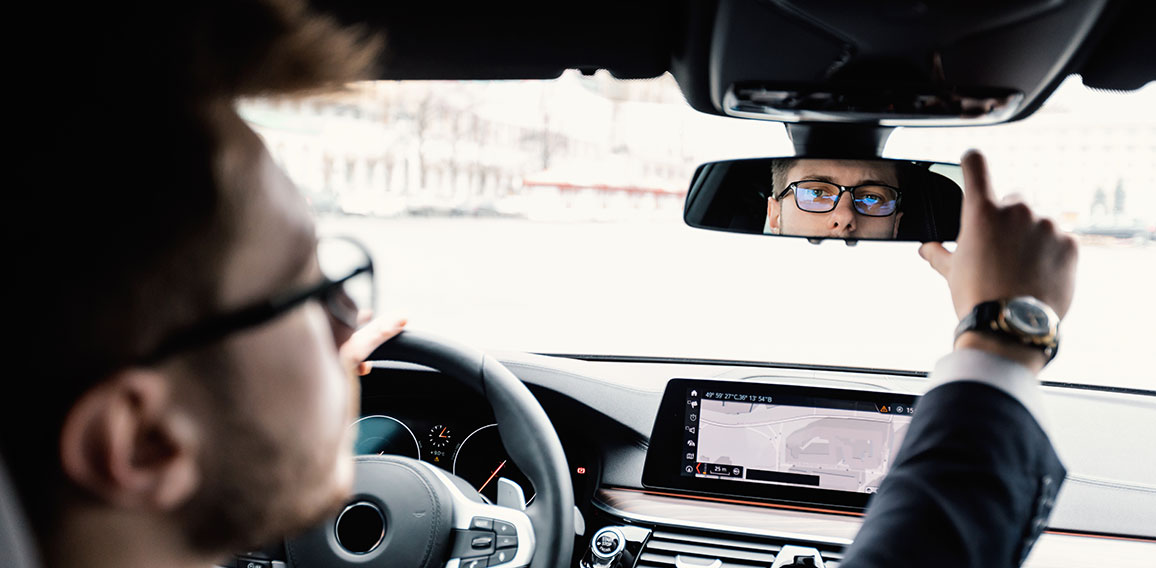 Young businessman driving alone adjusting rearview mirror