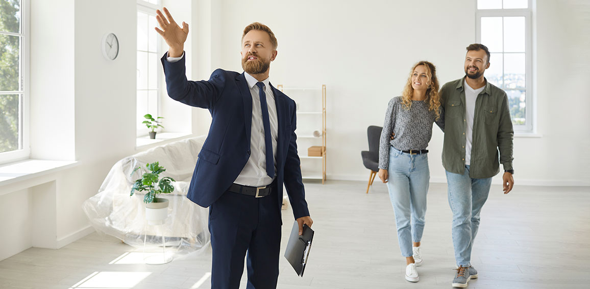 Real estate agent giving happy young customers a tour about a new spacious house