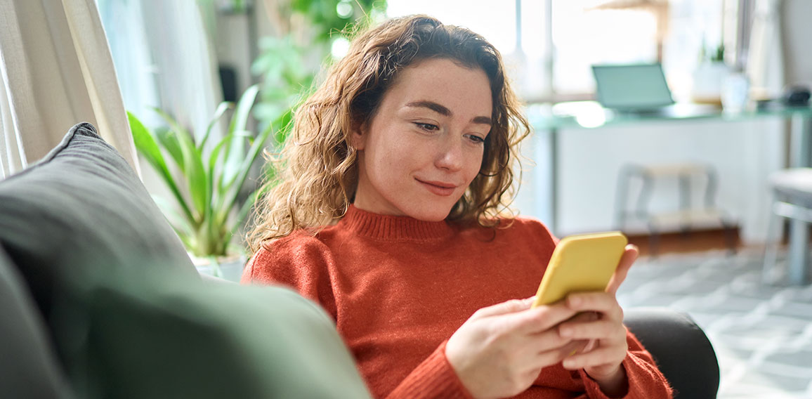 Smiling relaxed young woman sitting on couch using mobile phone technology.