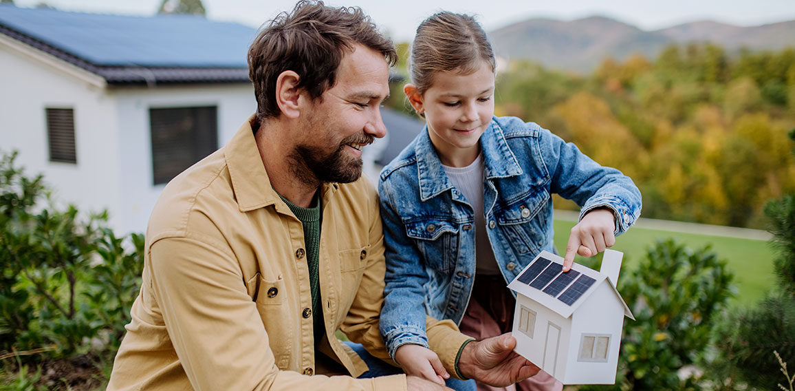 Little girl with her dad holding paper model of house with solar panels, explaining how it works.Alternative energy, saving resources and sustainable lifestyle concept.