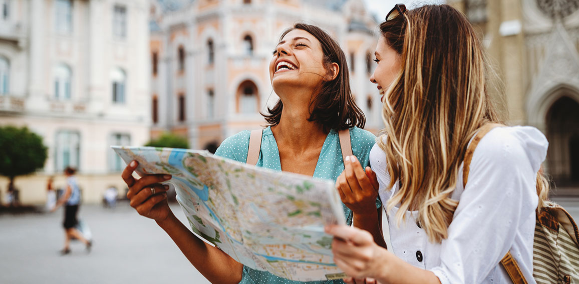 Fun, friends, travel and tourism concept. Beautiful girls looking for direction in the city