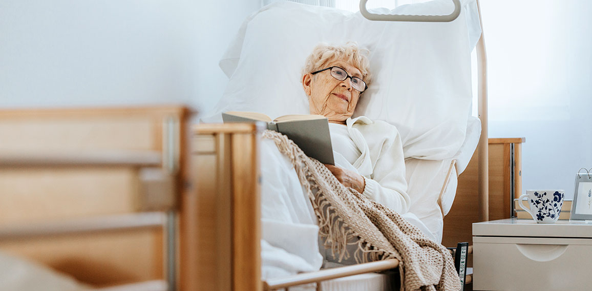 Sick senior woman lies in a hospital bed and reads a book