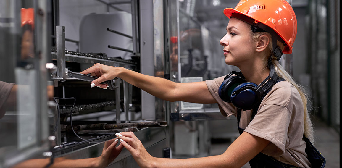 Serious female repairing broken equipment in factory using wrench, in uniform