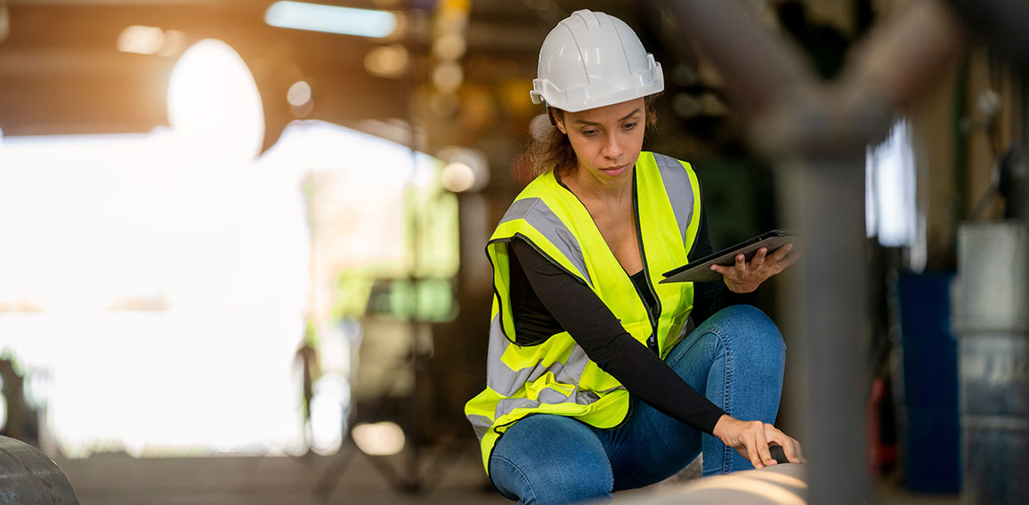 Young female in protective uniform inspecting industrial machine