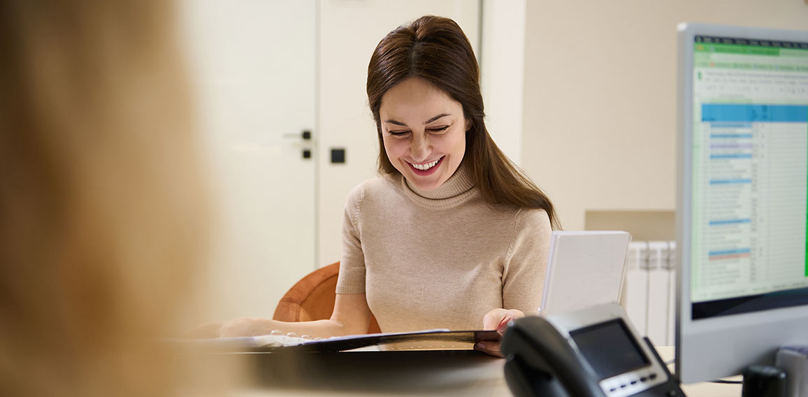 Beautiful woman leafing through a catalog of beauty procedures, checking the price-list in a folder with documents standing at wellness spa reception area