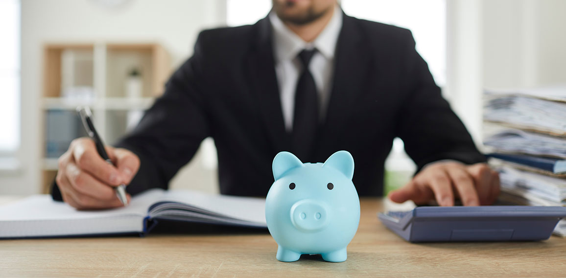 Piggy bank on desk of accountant who uses calculator to analyze budget and make calculations.