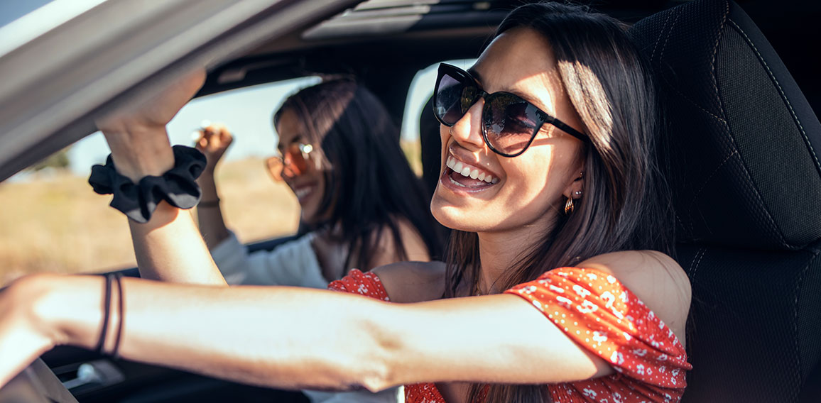 Pretty young women singing while driving a car on road trip on b