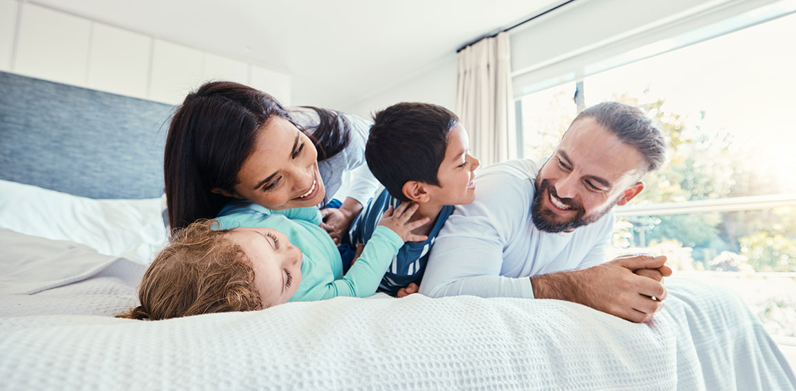 Happy, love and family being playful on the bed together in the bedroom of their modern house. Happiness, excited and children having fun, playing and bonding with their parents in a room at home.