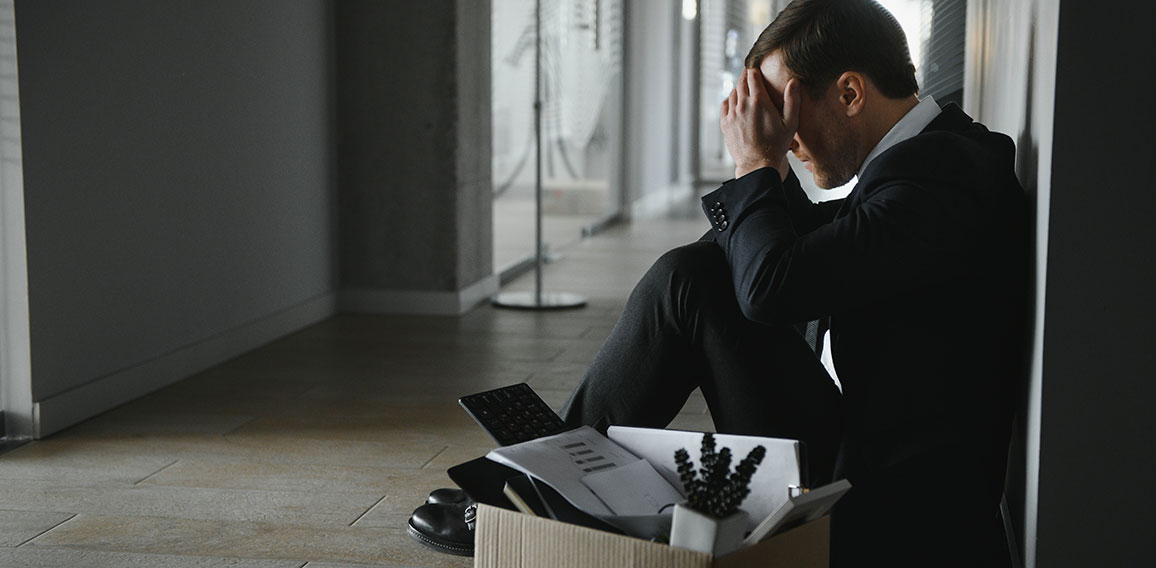 Sad fired businessman sitting outside meeting room after being dismissed.