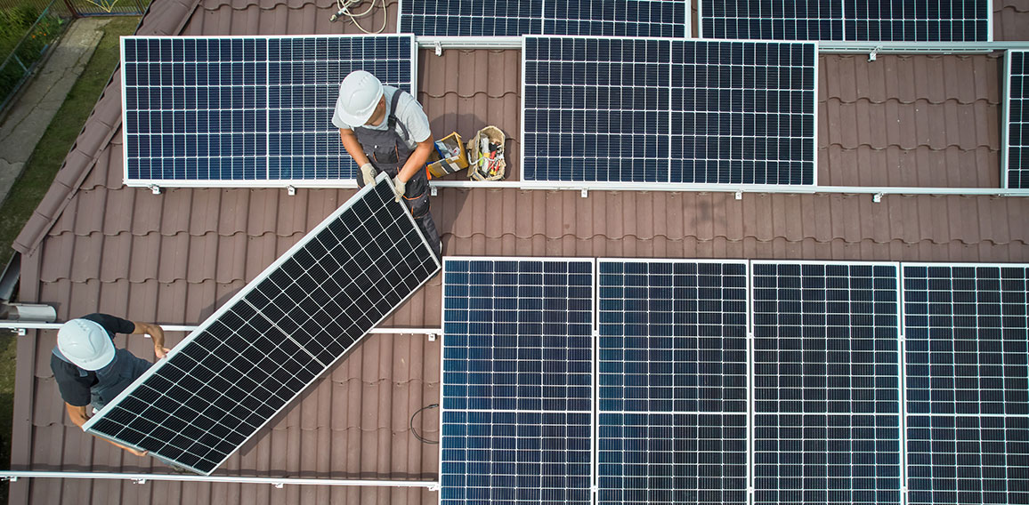 Men technicians mounting photovoltaic solar moduls on roof of house.