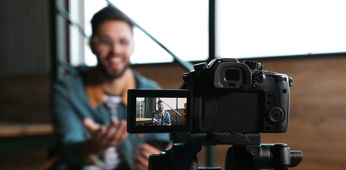 Young blogger recording video indoors, focus on camera screen