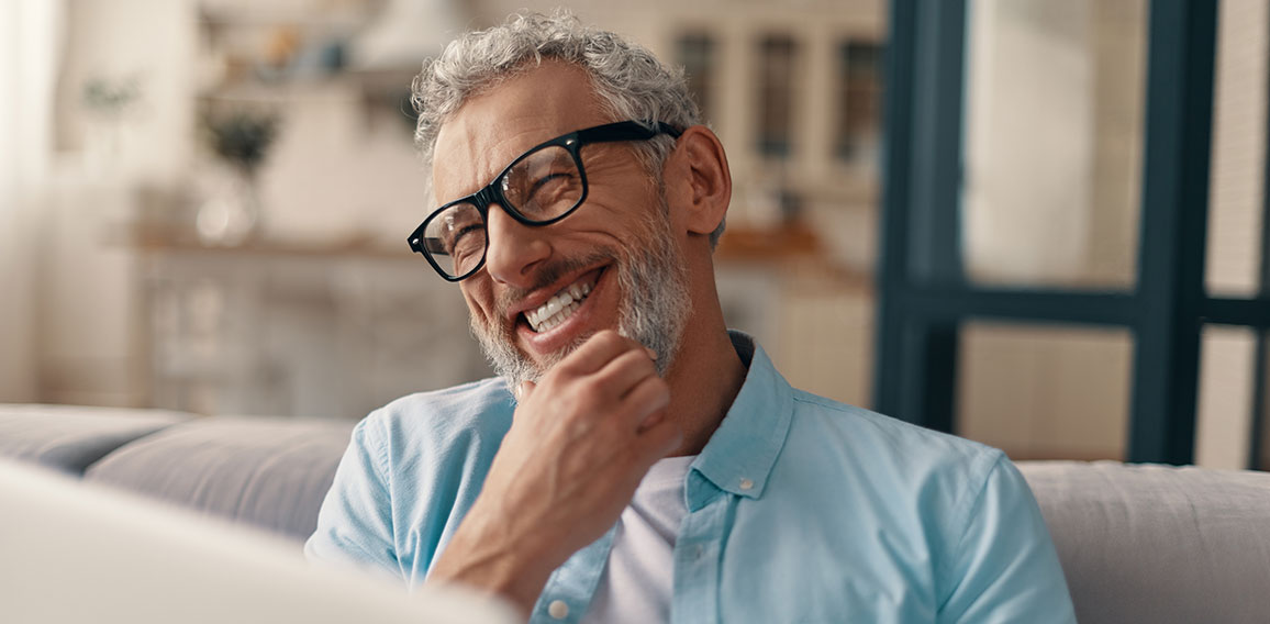 Cheerful senior man in casual clothing and eyeglasses using lapt