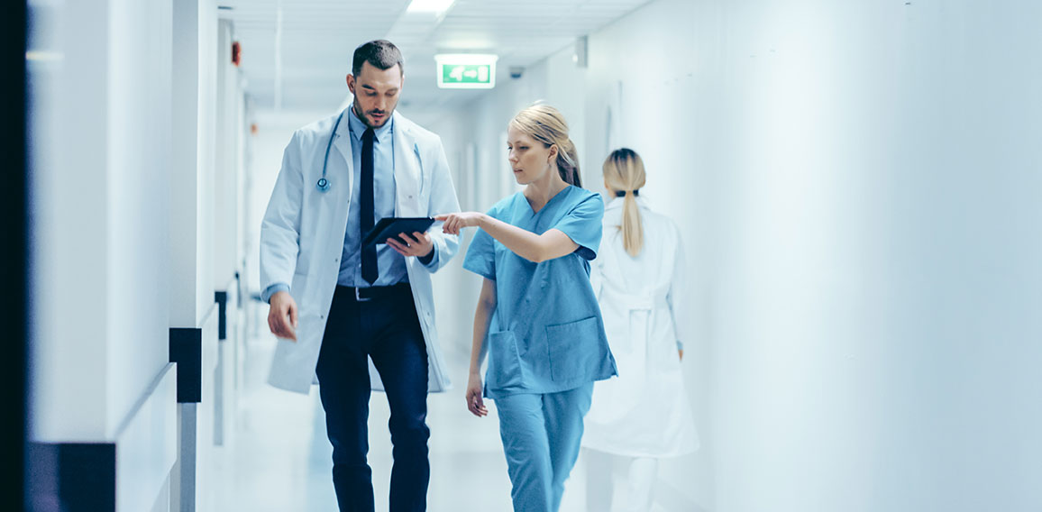 Female Surgeon and Doctor Walk Through Hospital Hallway, They Co