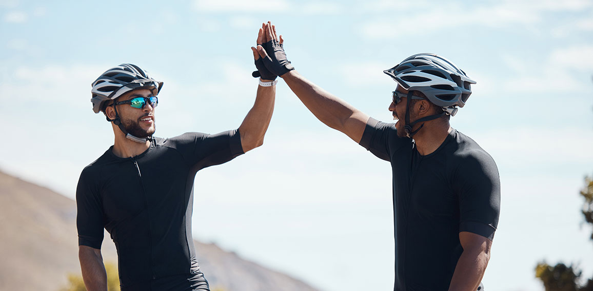 High five, winner and cycling team of cyclists having fun riding together outdoors in nature. Happy, excited and fit male bicycle riders on a break after exercising and training in the environment