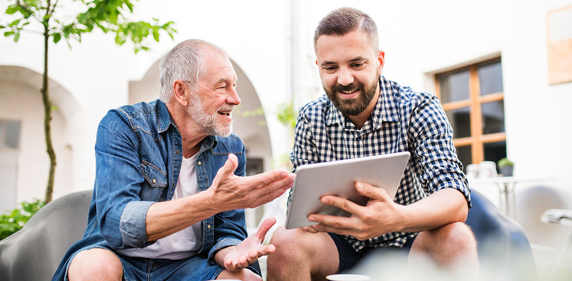 An adult hipster son with tablet and senior father in a cafe in town.