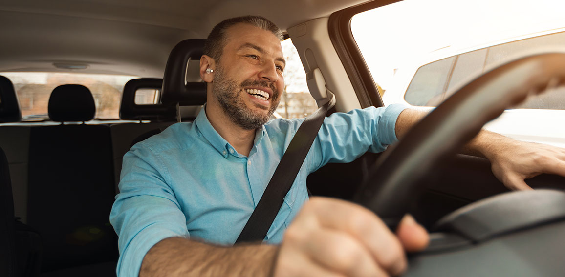 Happy man in earphones enjoying music driving luxury car